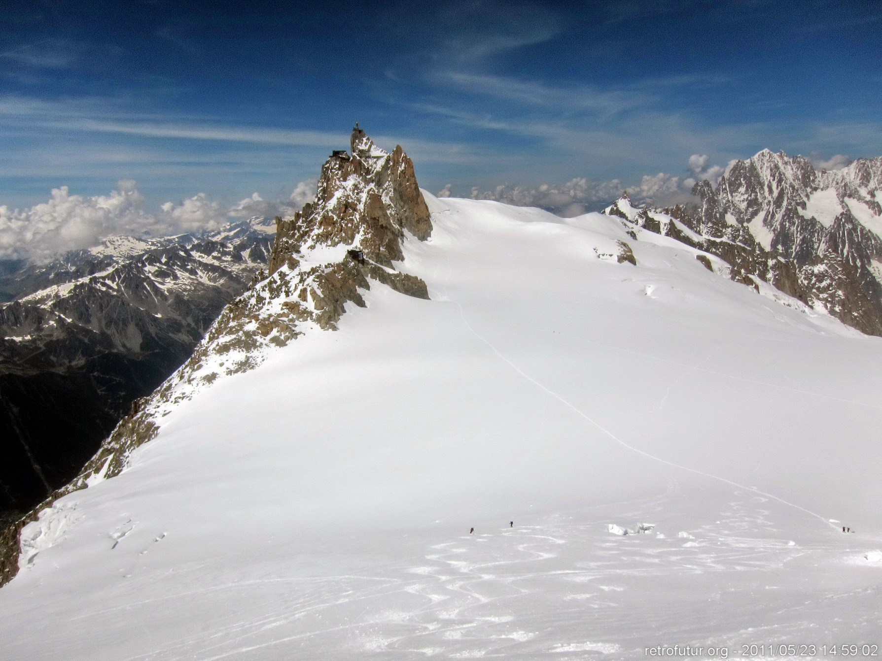 Tag 2: Aklimatisierung : 14:49 - Einfach laufen lassen. Zöpfe flechten hinab zum Col du Midi (3532m). In den Himmel ragt die Bergstation der Aiguille Du Midi mit Seilbahn (3842 m), darunter über dem Gletscherplateau unsere Herberge für die Nacht, das Refuge des Cosmiques (3613m)