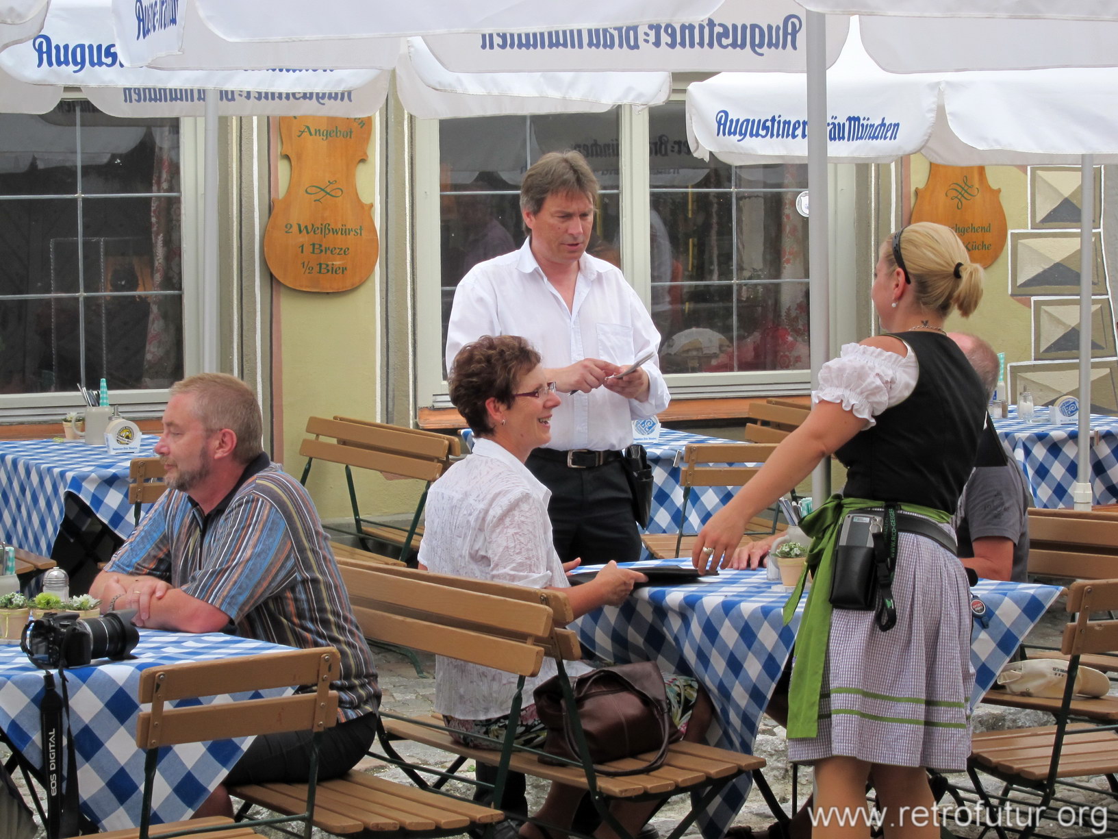 Mittenwald im Speziellen und das Umland im Allgemeinen : Gast mit Spiegelreflexkamera (links) und Bestellaufnahmevorgang bei einem weiteren Gast. Bedienung in Kleidung mit lokaltypischen Elementen.